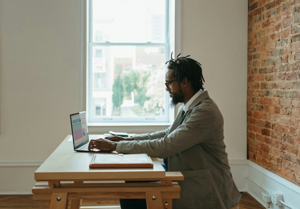 Person reviewing information on a laptop beside documents at a desk.